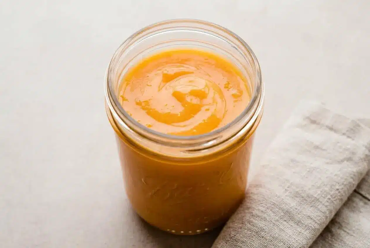 A small white bowl filled with the finished orange curd recipe, showing its silky, bright orange surface with a spoon resting inside.