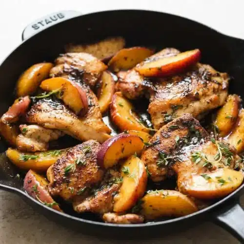 Peach chicken in a cast iron skillet, with golden seared chicken thighs and tender peaches in a glossy honey lemon sauce.