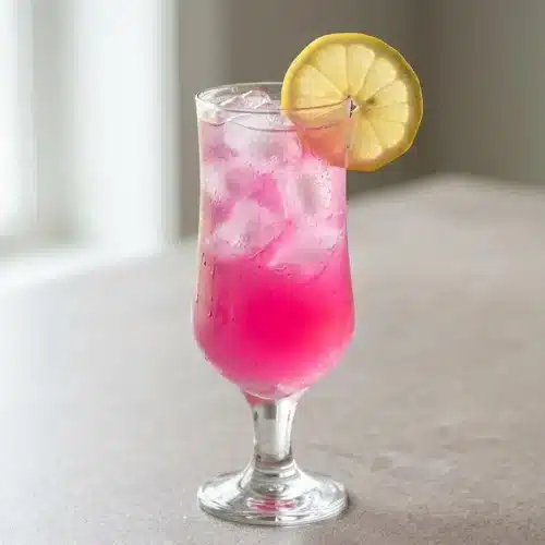 A tall glass and pitcher of vibrant, refreshing Prickly Pear Lemonade, garnished with fresh lemon slices and filled with ice.