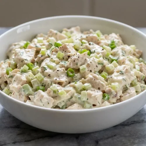 A bowl of creamy rotisserie chicken salad made with a crème fraîche dressing, garnished with fresh dill and celery.