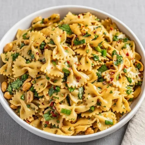 A large white bowl of Spicy Thai Pasta Salad with bowtie pasta, cilantro, and peanuts, all coated in a glossy sesame dressing.