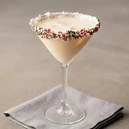A creamy Sugar Cookie Martini in a glass with a festive sprinkle and frosting rim.
