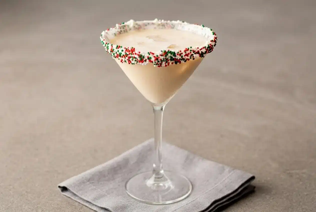 A creamy Sugar Cookie Martini in a glass with a festive sprinkle and frosting rim.
