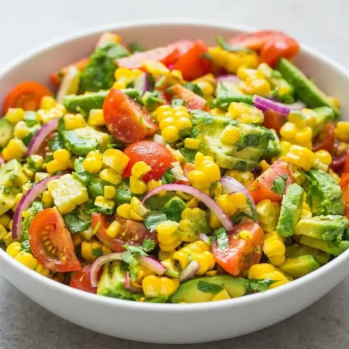 A large white bowl of Summer Corn Salad with Avocado, showing charred corn, creamy avocado slices, and juicy cherry tomatoes.