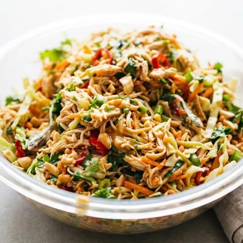 A large bowl of Thai Chicken Salad with shredded chicken, crunchy cabbage, and carrots, all tossed in a creamy peanut dressing.