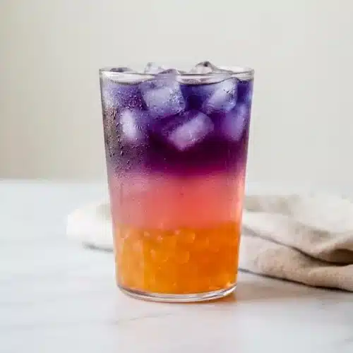 A tall glass of a layered Tropical Butterfly Refresher recipe with mango boba, a pink guava layer, and a vibrant blue top.