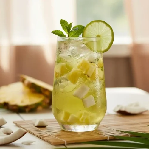 A tall glass of tropical iced green tea recipe, filled with ice cubes and pineapple bits, showing its clear, refreshing yellow-green color.