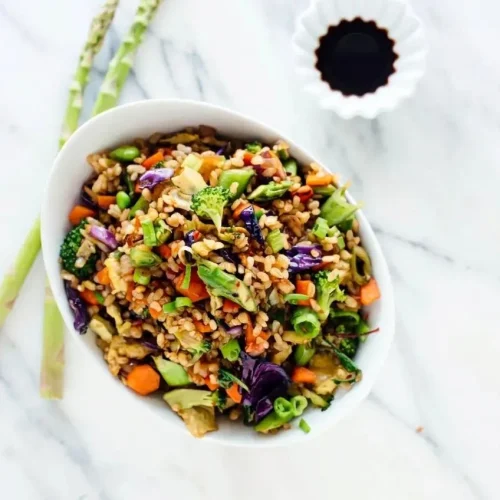 A large skillet filled with vegetable fried rice, showing distinct brown rice grains, scrambled egg, and colorful chopped vegetables.