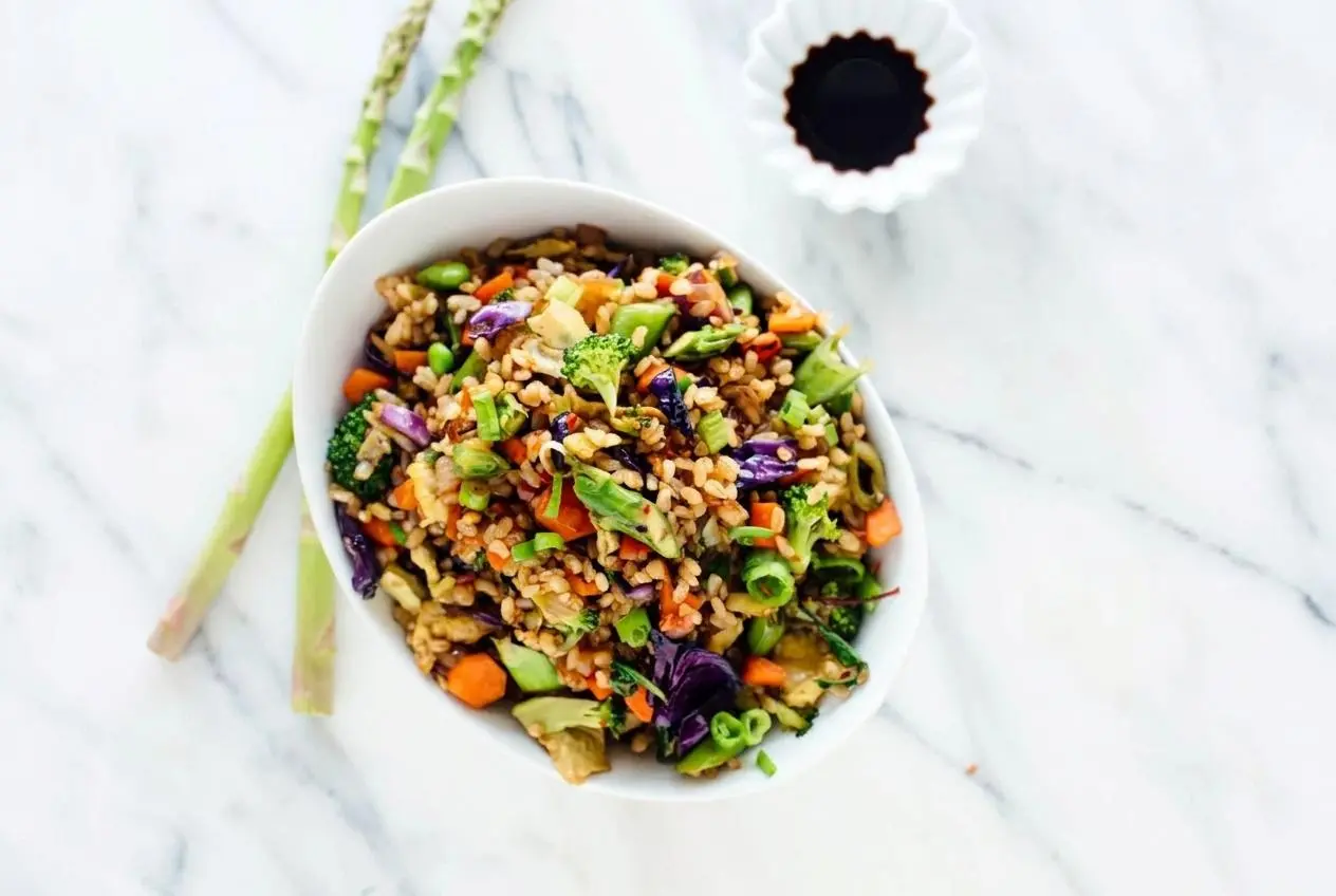 A large skillet filled with vegetable fried rice, showing distinct brown rice grains, scrambled egg, and colorful chopped vegetables.