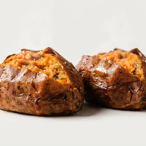 A whole air fryer baked sweet potato with crispy, salt-flecked skin, split open to reveal the fluffy, bright orange flesh inside.