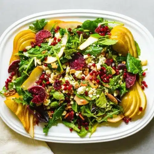 A large shallow bowl of blood orange salad with baby kale, arugula, juicy red orange segments, crumbled gorgonzola, and walnuts.