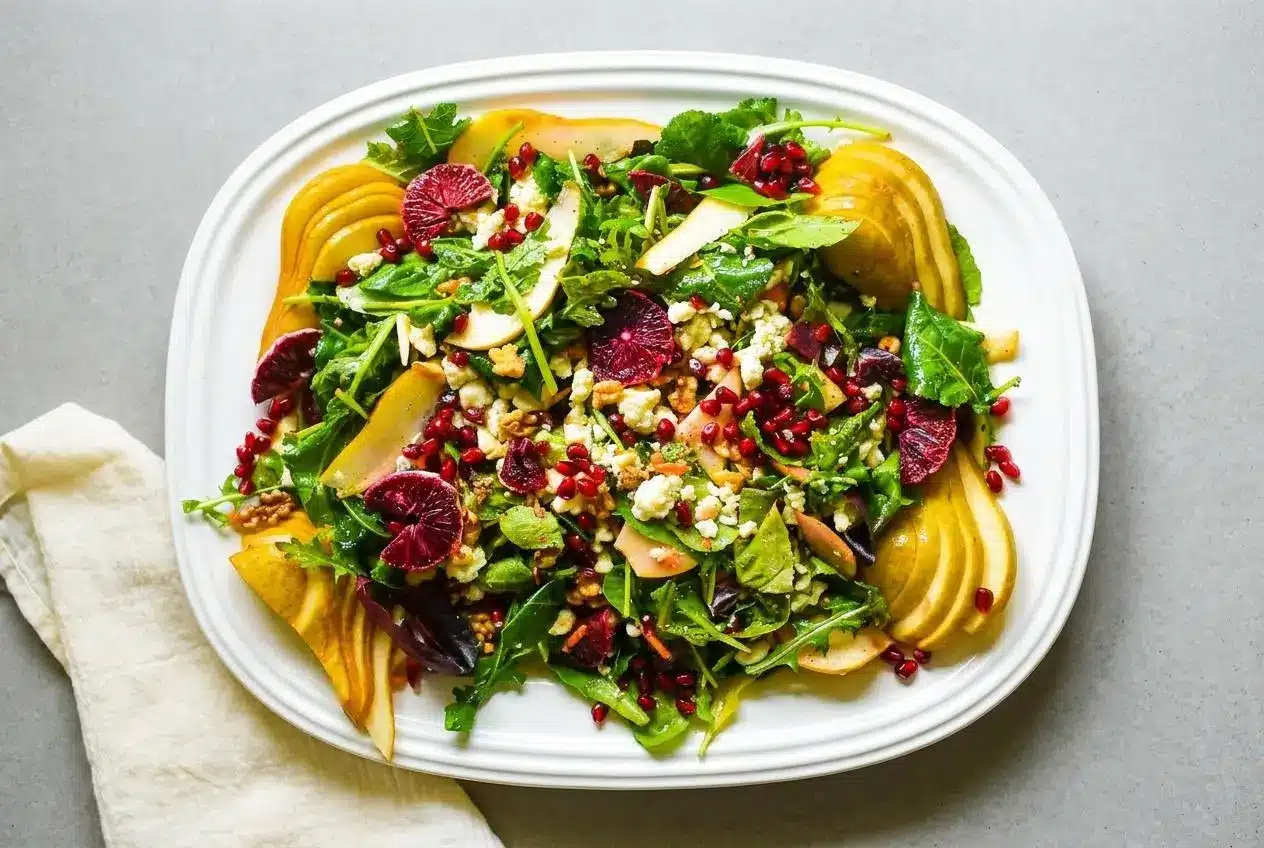 A large shallow bowl of blood orange salad with baby kale, arugula, juicy red orange segments, crumbled gorgonzola, and walnuts.