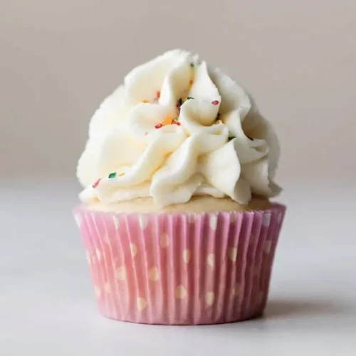 A large glass bowl of smooth, fluffy buttercream frosting, with an offset spatula creating a deep swirl to show its pipeable texture.