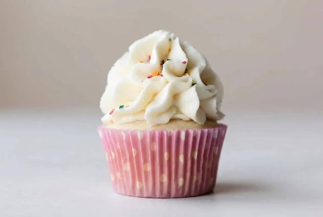 A large glass bowl of smooth, fluffy buttercream frosting, with an offset spatula creating a deep swirl to show its pipeable texture.