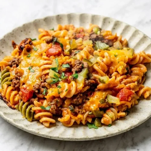 A white baking dish of cheeseburger casserole with a bubbly, golden-brown melted cheddar cheese topping and a sprinkle of chopped dill