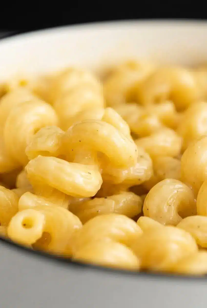An extreme close-up of cavatappi pasta, showing the perfectly smooth and velvety texture of the cheese sauce with flecks of black pepper.