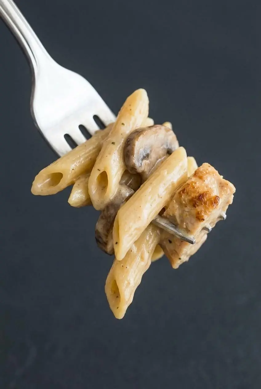 A close-up of a fork twirling pasta to show the smooth, glossy texture of the creamy mushroom sauce, which is not grainy or split.