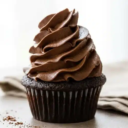 A white bowl filled with a rich, fluffy chocolate frosting recipe, with an offset spatula lifting a smooth scoop.