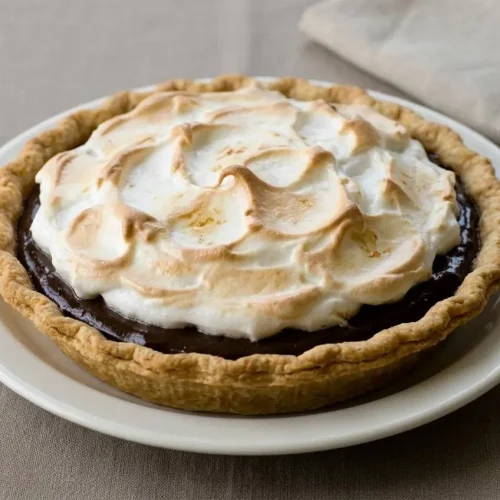 A whole chocolate pie recipe in a glass dish, showing the silky chocolate custard filling beneath a fluffy, toasted meringue topping.