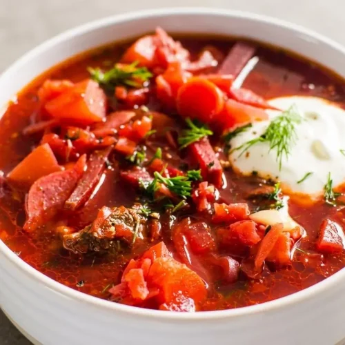 A bowl from a classic borscht recipe, showing the ruby-red beet soup topped with a dollop of sour cream and fresh dill.