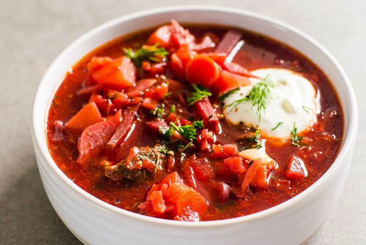 A bowl from a classic borscht recipe, showing the ruby-red beet soup topped with a dollop of sour cream and fresh dill.
