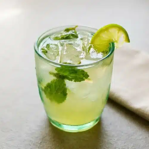 A refreshing coconut water mocktail in a rocks glass with ice, muddled mint leaves, and a fresh lime wedge garnish.