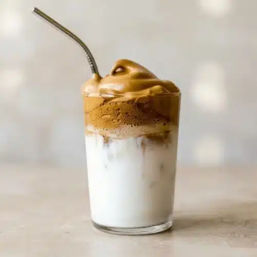 A tall glass of Coconut Whipped Coffee, showing fluffy light-brown coffee foam layered over icy white coconut milk.