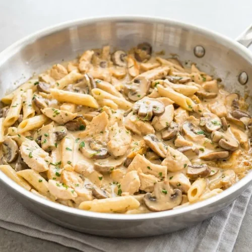A bowl of Chicken Mushroom Pasta with a glossy cream sauce, tender chicken, sliced mushrooms, and a sprinkle of fresh parsley.