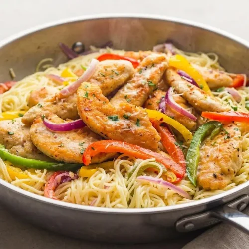A white bowl of creamy chicken scampi with angel hair pasta, golden chicken tenders, and sliced bell peppers, garnished with fresh parsley.