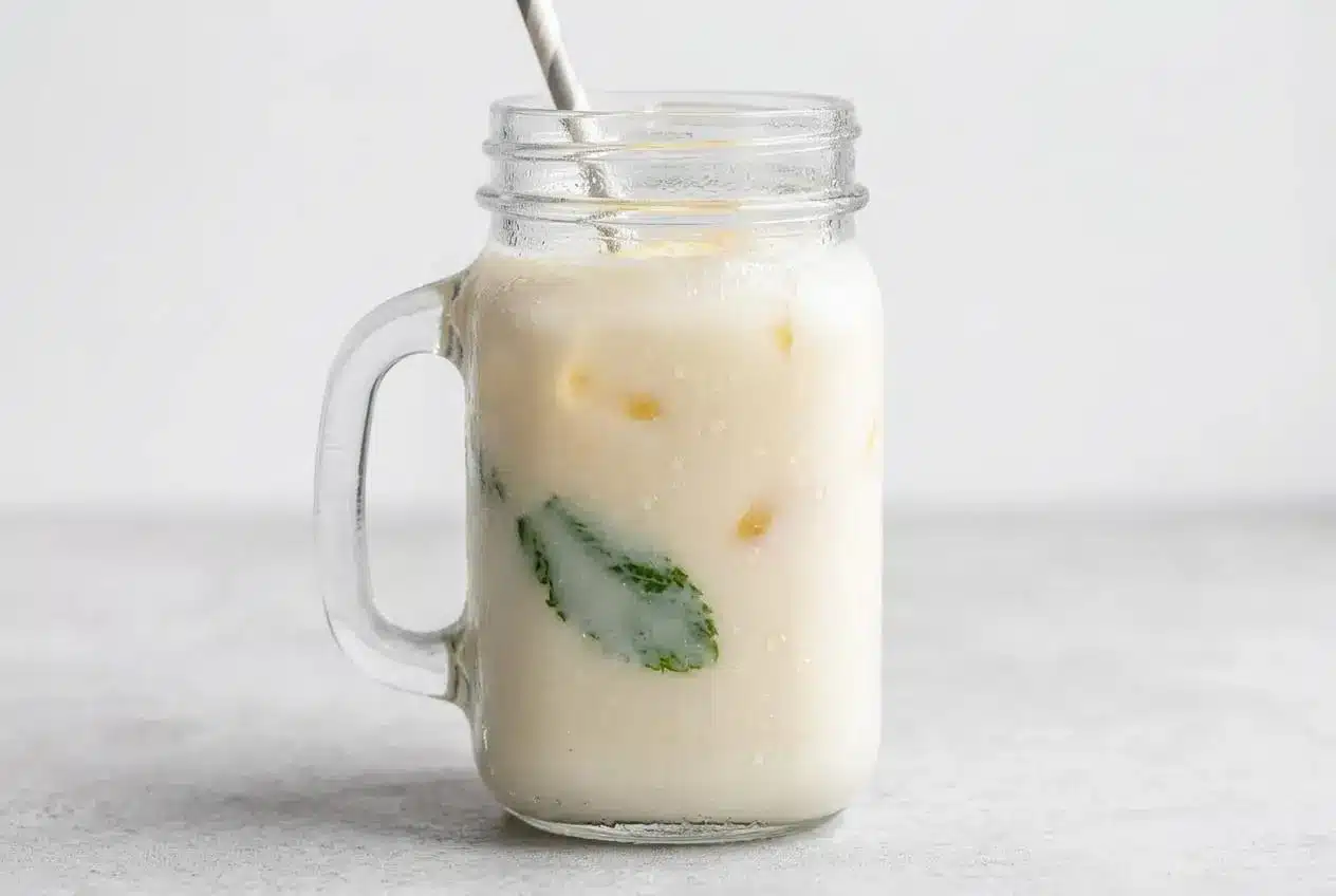 A tall glass of creamy lemonade with a velvety smooth texture, garnished with a lemon slice and mint sprig, next to a pitcher.
