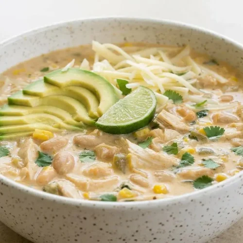 A blue bowl of creamy White Bean Chicken Chili topped with fresh cilantro, a lime wedge, and tortilla strips.