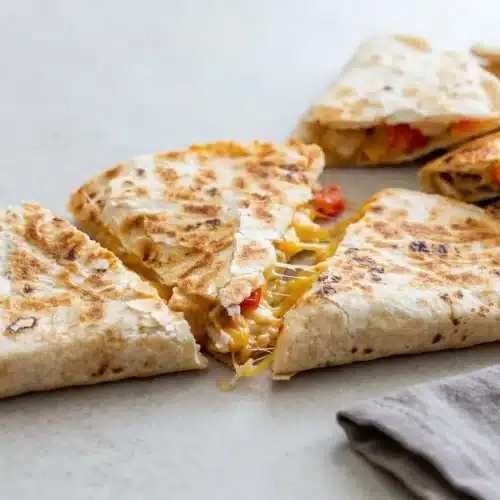 Golden-brown chicken quesadillas cut in wedges and stacked to show the cheesy chicken and pepper filling.