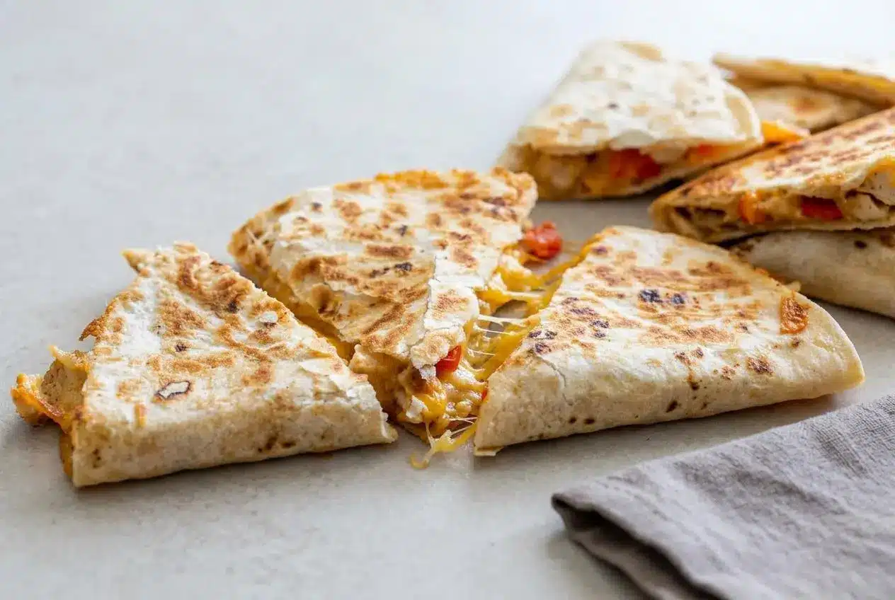 Golden-brown chicken quesadillas cut in wedges and stacked to show the cheesy chicken and pepper filling.