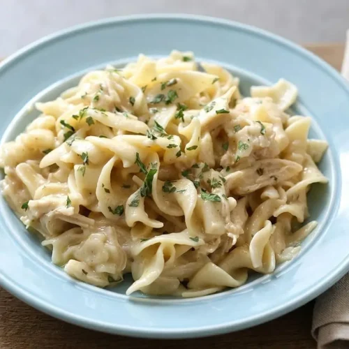 A bowl of creamy Crockpot Chicken and Noodles with tender shredded chicken, egg noodles, and a sprinkle of parsley.
