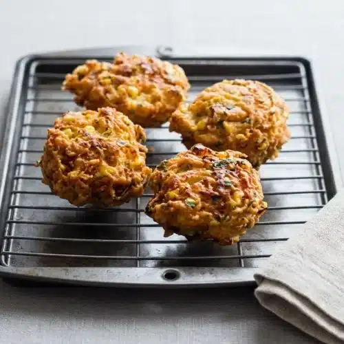 A close-up stack of golden brown, crispy corn fritters from an easy recipe, piled on a rustic plate.