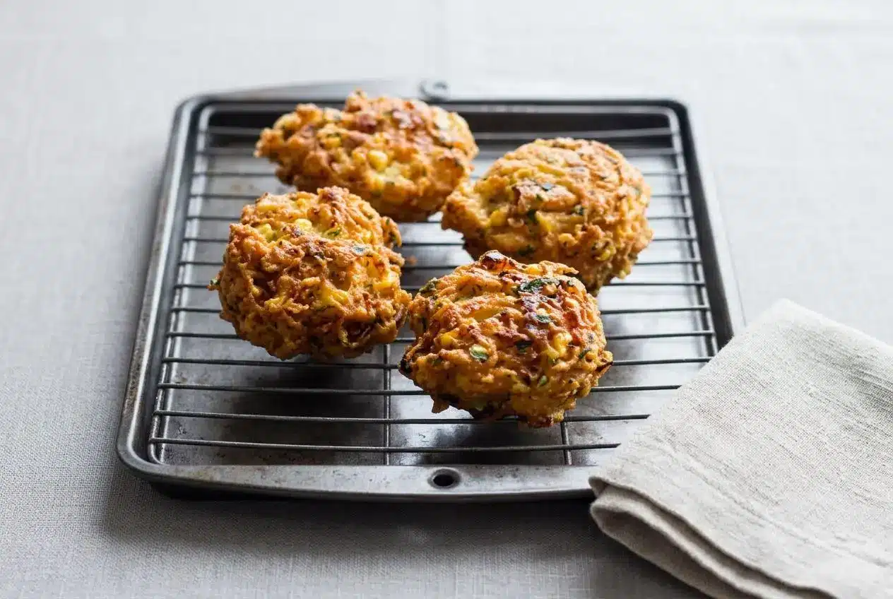 A close-up stack of golden brown, crispy corn fritters from an easy recipe, piled on a rustic plate.