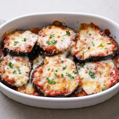 A rectangular white baking dish of eggplant casserole with a bubbly, golden-brown mozzarella and Parmesan topping.