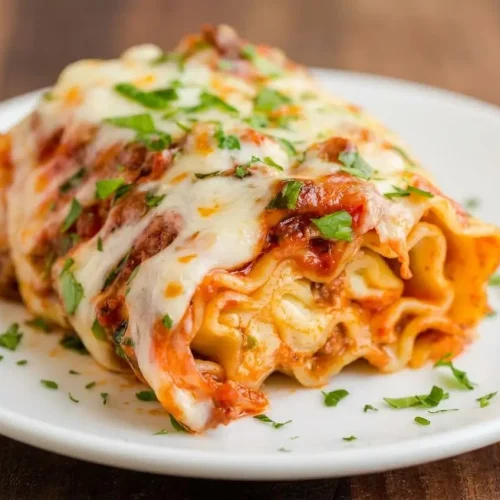 A casserole dish of lasagna roll ups with a savory meat sauce and a golden brown, bubbly mozzarella cheese topping, garnished with fresh