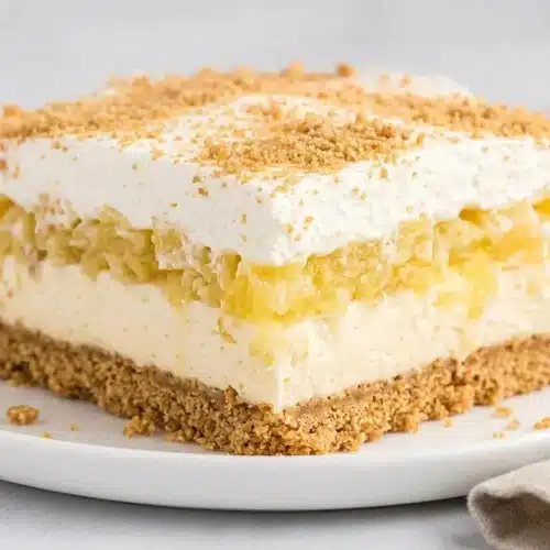 A sliced square of Pineapple Dream Dessert showcasing distinct layers of graham crust, cream cheese, and whipped topping.