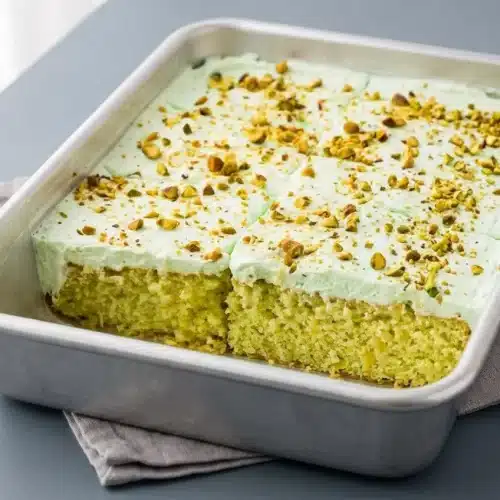 A slice of Pistachio Pineapple Cake showing the moist crumb and fluffy pale green whipped frosting.