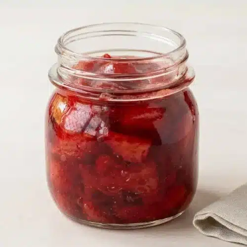 A white bowl filled with chunky strawberry compote, showing soft red fruit pieces in a glossy syrup.