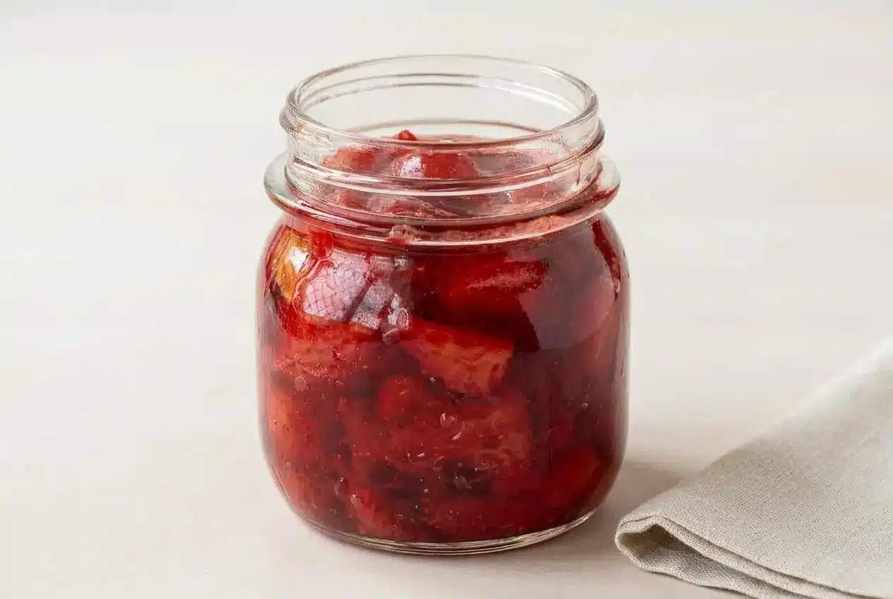 A white bowl filled with chunky strawberry compote, showing soft red fruit pieces in a glossy syrup.