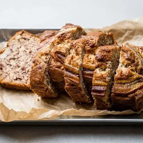 A whole loaf of Greek yogurt banana bread with a golden-brown, cracked top, resting on a dark surface.