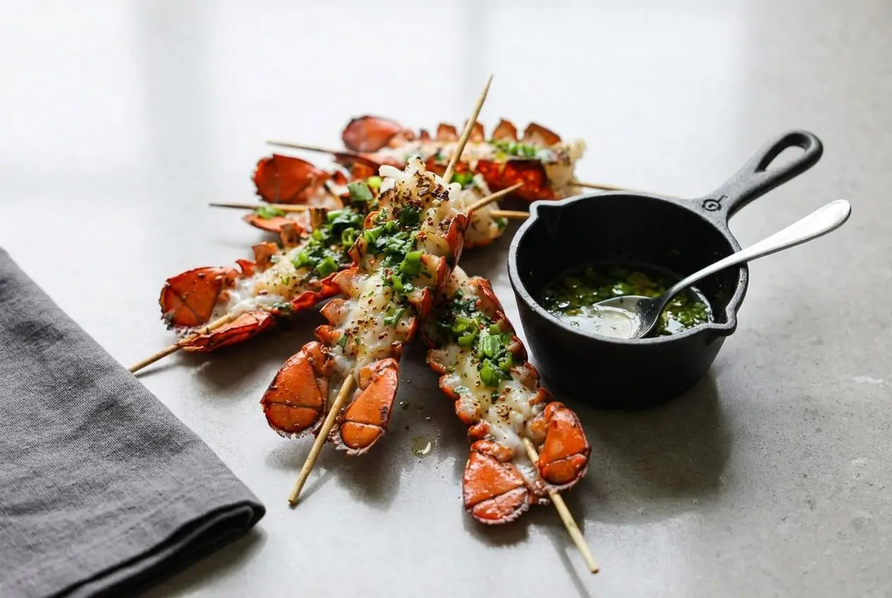 Grilled lobster skewers drizzled with a creamy Bang Bang sauce and topped with fresh cilantro on a dark platter.