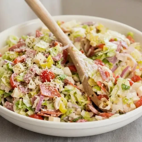 A large white bowl of grinder salad recipe, with finely chopped lettuce, deli meats, and cheese tossed in a creamy, tangy dressing.