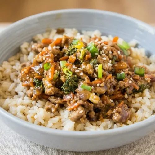 A white bowl of Ground Turkey Rice Bowls, showing savory ground turkey with broccoli and carrots in a glossy teriyaki sauce over rice