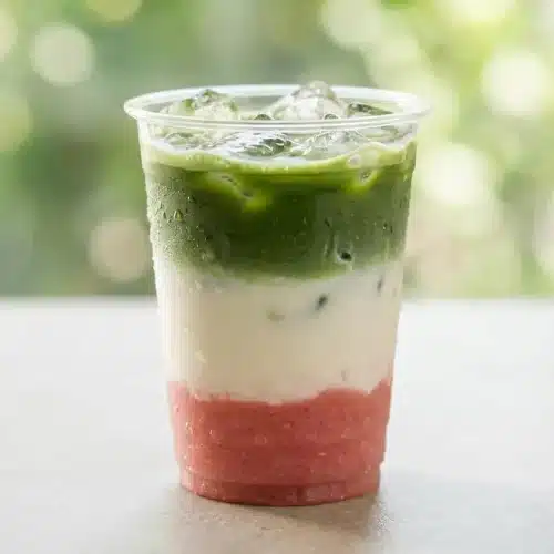 A layered Guava Matcha Latte in a tall glass, showing a pink guava base, a creamy white milk middle, and a vibrant green matcha top.