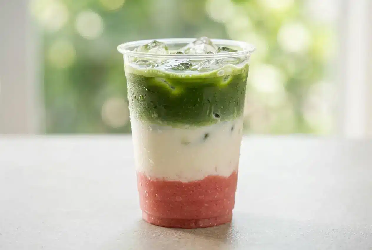 A layered Guava Matcha Latte in a tall glass, showing a pink guava base, a creamy white milk middle, and a vibrant green matcha top.