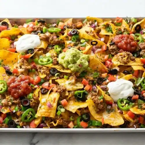 A sheet pan of the finished Loaded Nachos Recipe, topped with seasoned ground beef, melted cheese, tomatoes, and green onions.