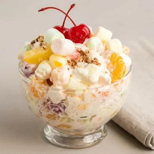 A glass bowl filled with creamy Marshmallow Fruit Salad, showing mandarin oranges, pineapple, and colorful mini marshmallows.